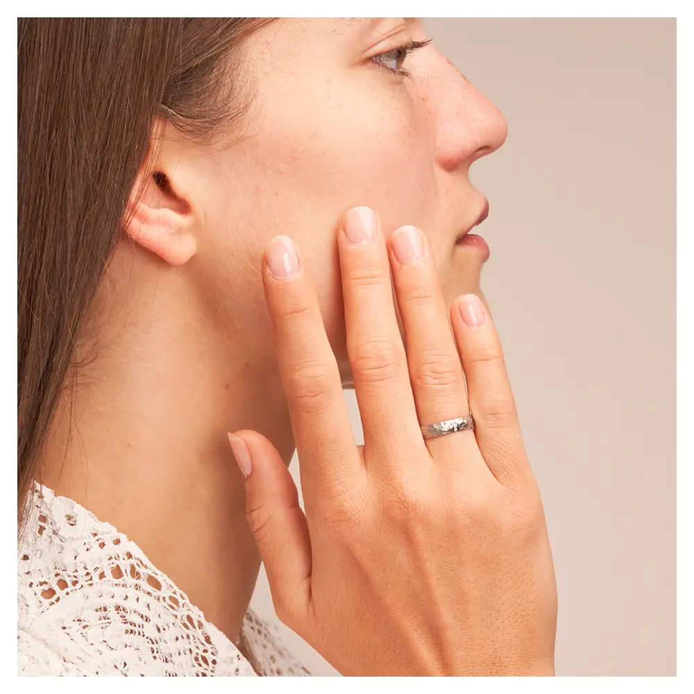 Eheringen aus Edelstahl mit gehämmerter Oberfläche und drei Diamanten auf Hand am Gesicht