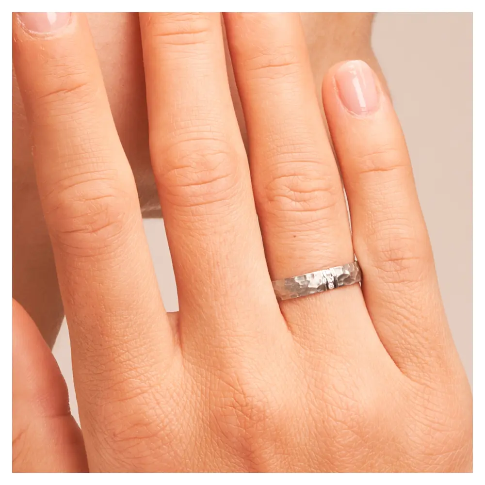 Eheringen aus Edelstahl mit gehämmerter Oberfläche und drei Diamanten auf Hand am Gesicht im Zoom
