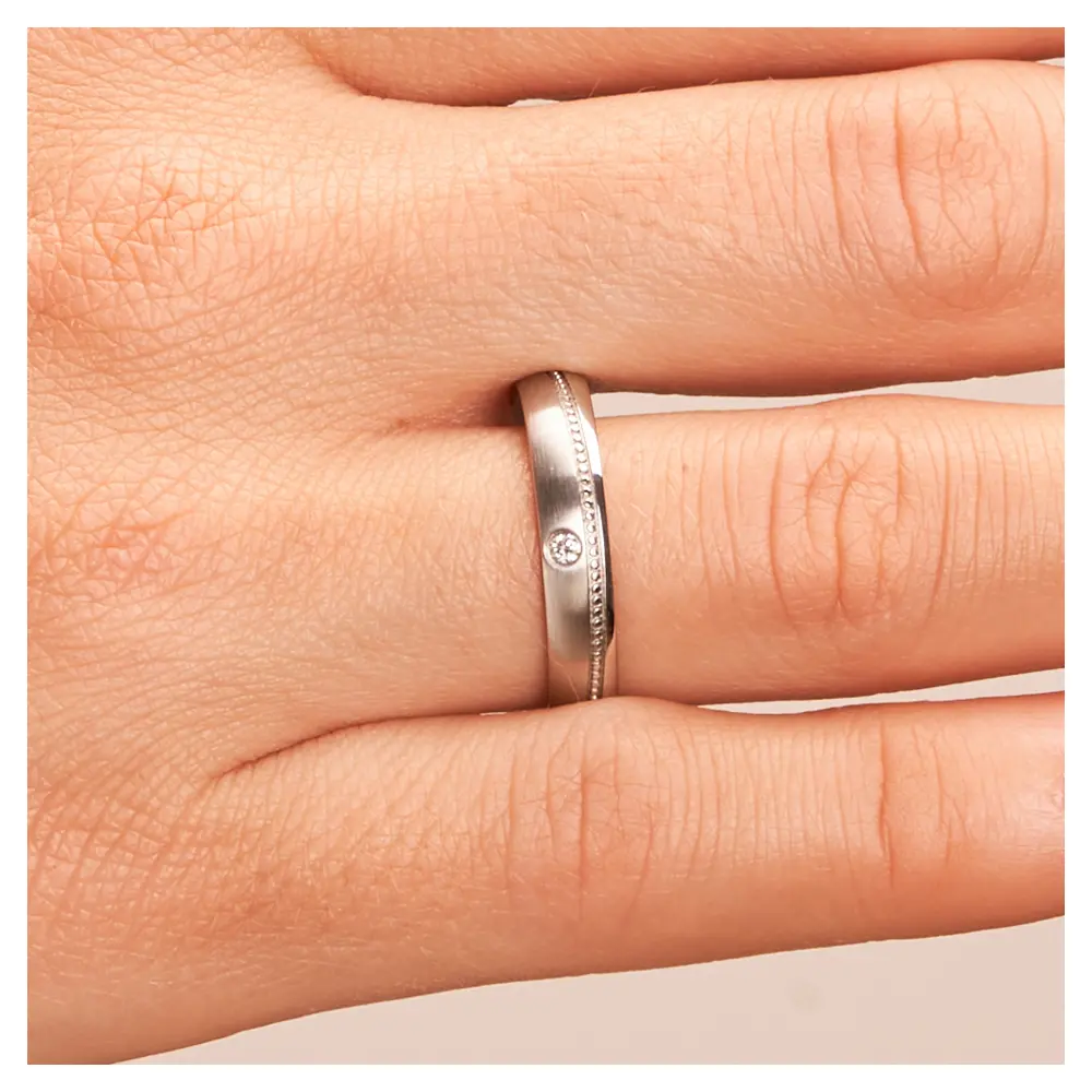 Eheringe aus Edelstahl mit Millgriff Muster und Diamanten auf Hand im Zoom