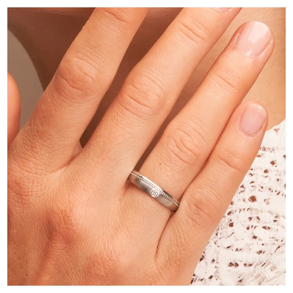 Eheringe aus Edelstahl mit Millgriff Muster und Diamanten auf Hand am Gesicht im Zoom