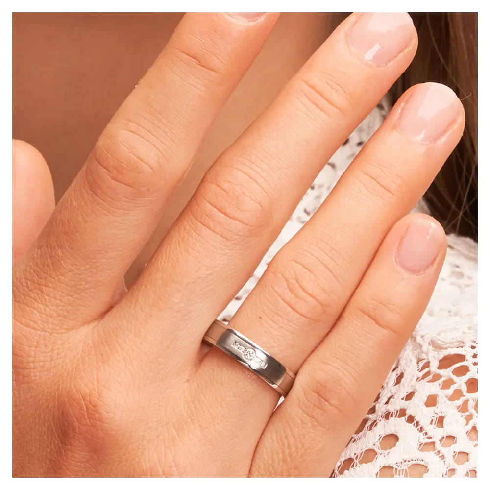 Edelstahl Trauringe längsmattiert mit vier kleinen und einem großen Diamanten auf Hand am Gesicht im