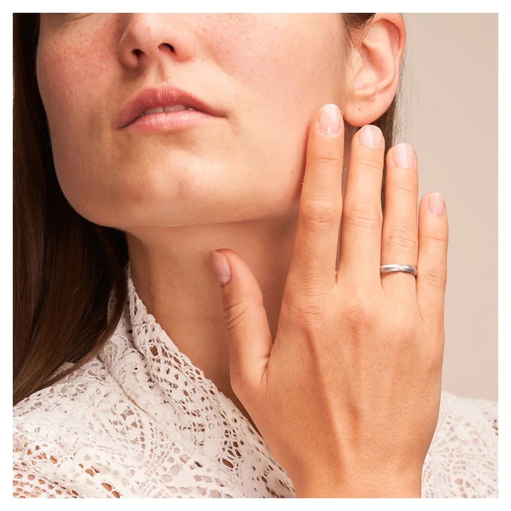 Trauringe aus quermattiertem Edelstahl mit Diamanten auf Hand am Gesicht