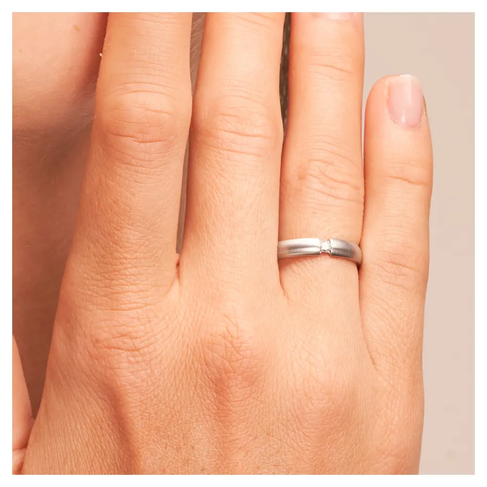 Trauringe aus quermattiertem Edelstahl mit Diamanten auf Hand am Gesicht im Zoom