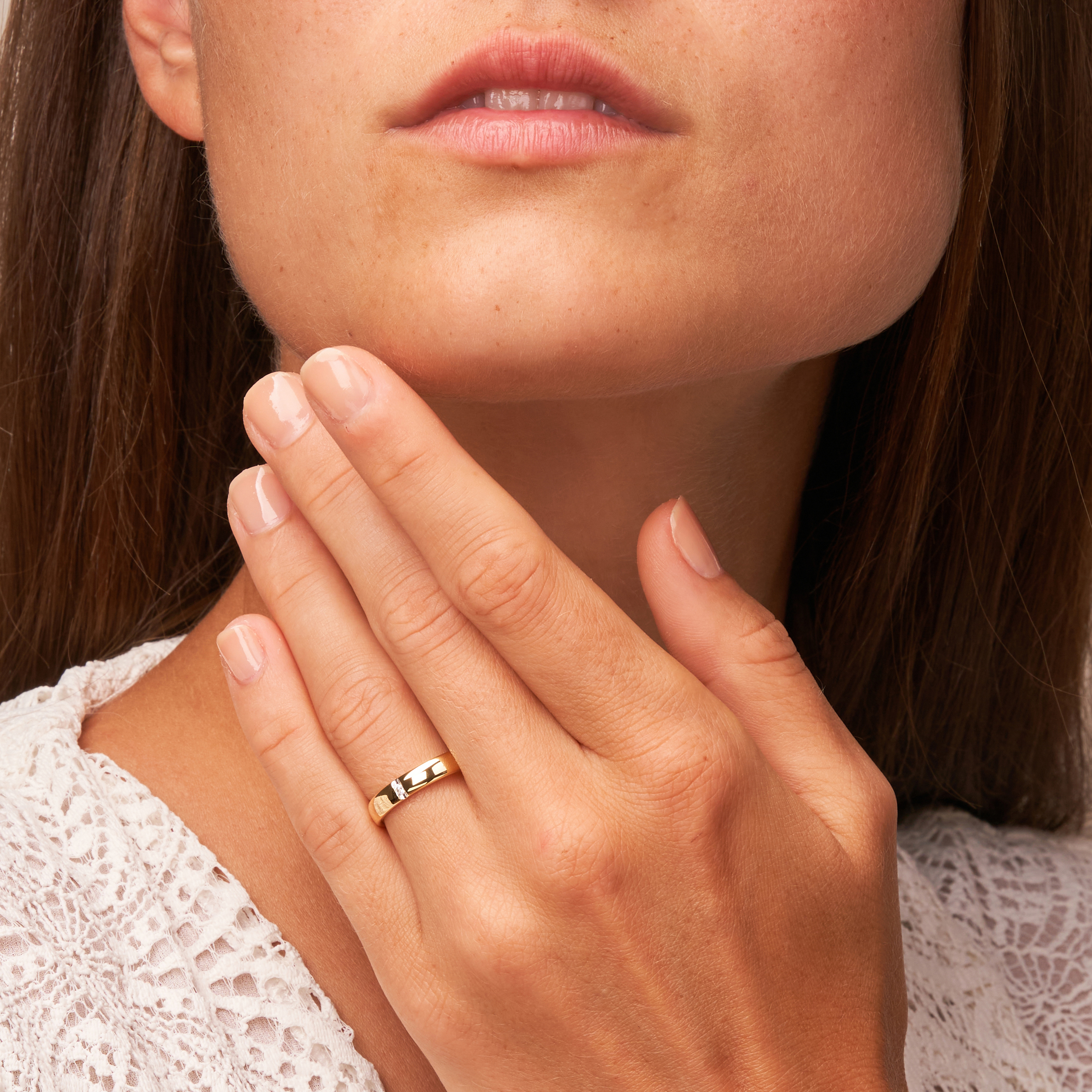 Eheringe aus Gelbgold mit Diamantbesatz und polierter Oberfläche auf Hand am Gesicht