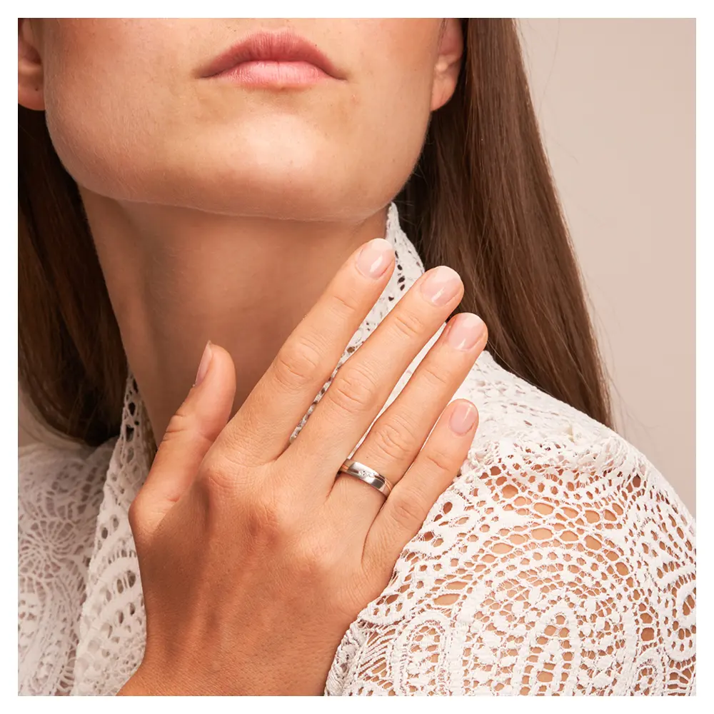 Trauring aus Edelstahl mit Roségoldstreifen und drei Diamanten auf Hand am Gesicht