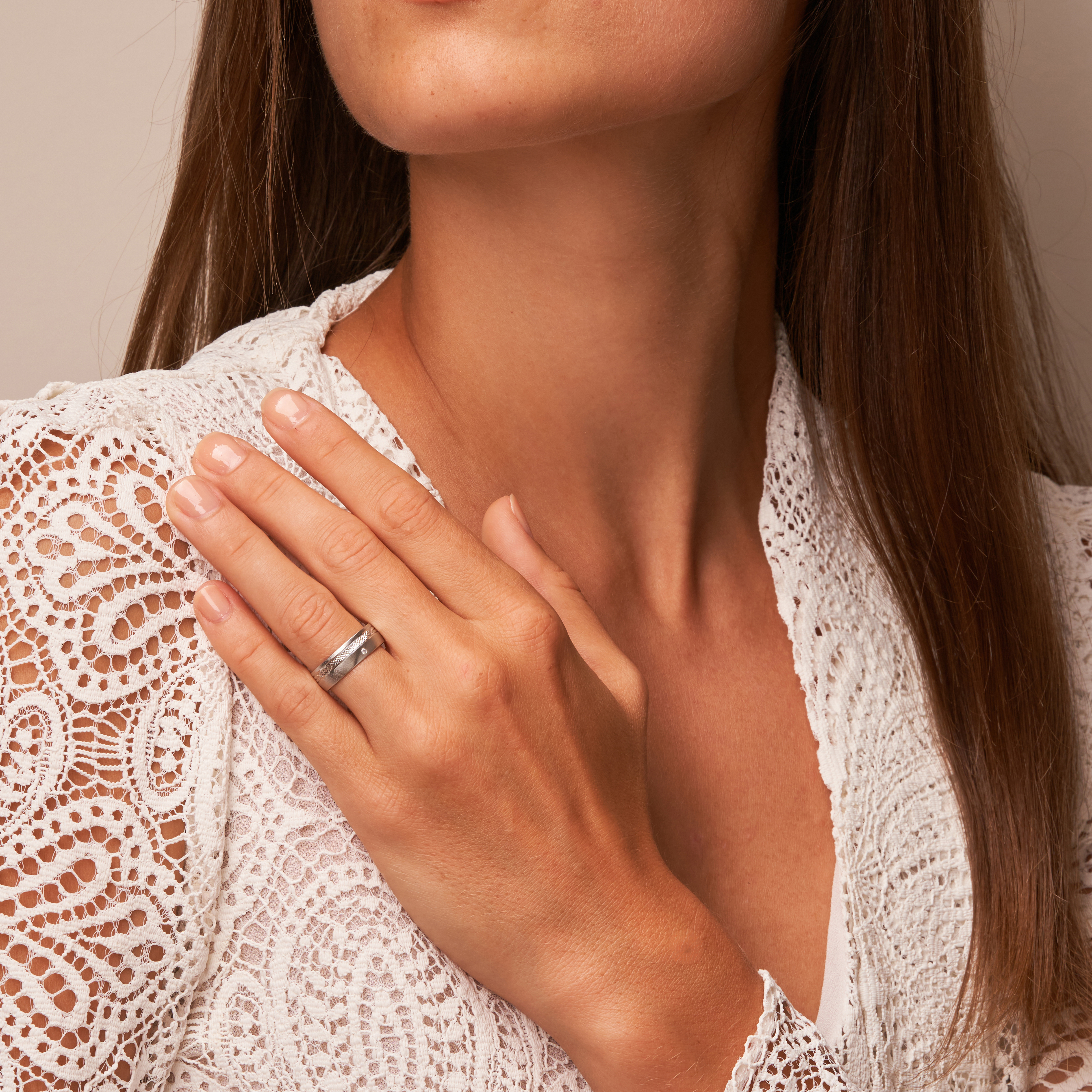 Quermattierter Platin Ehering mit gemustertem Streifen und Diamanten auf Hand am Gesicht