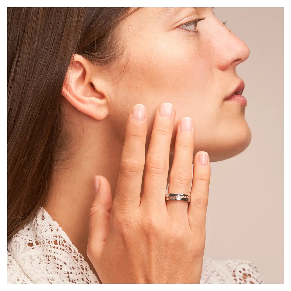 Trauring aus Edelstahl mit Roségoldstreifen und Diamanten auf Hand am Gesicht
