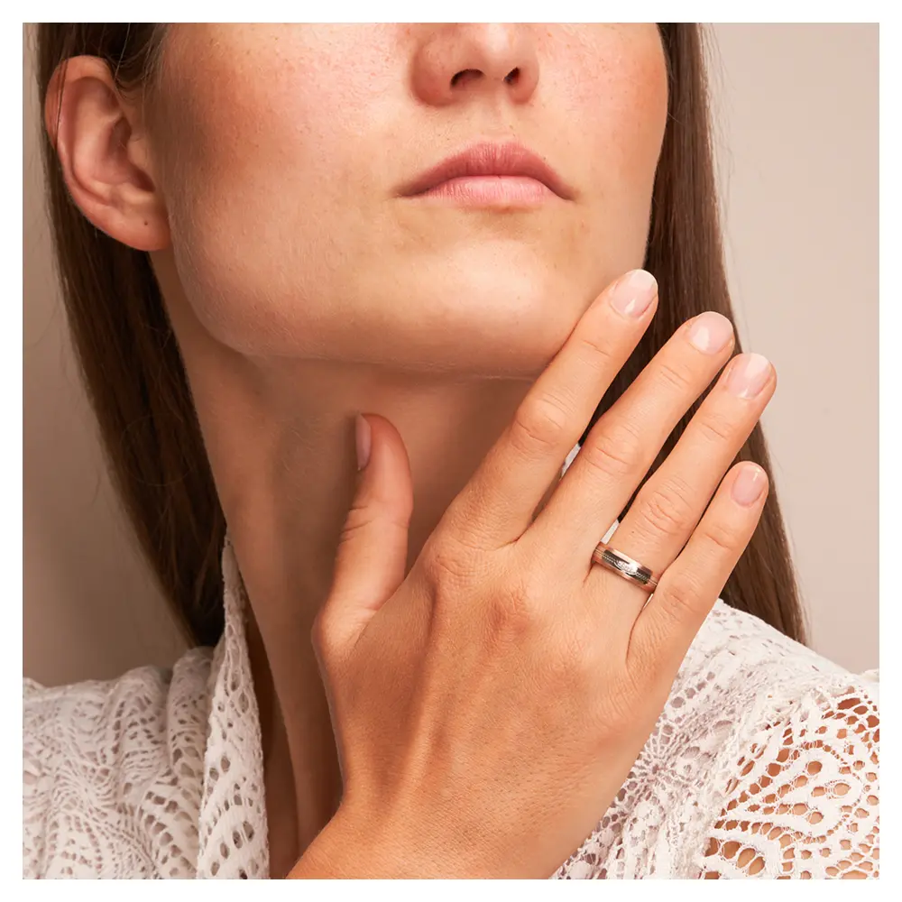 Ehering aus Edelstahl mit Roségoldrändern und drei Diamanten auf Hand am Gesicht