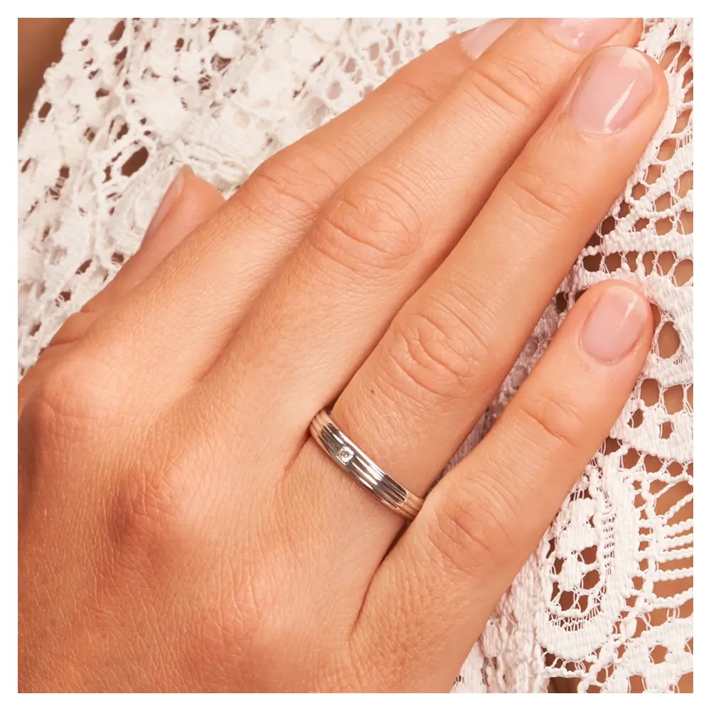 Strukturiert gestaltete Trauring aus 925 Silber mit Diamanten auf Hand am Gesicht im Zoom