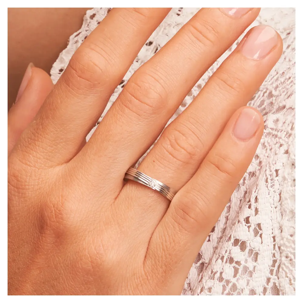 In Stufen gestaltete Eheringe aus 925er Silber mit Diamanten und Rillen auf Hand am Gesicht im Zoom