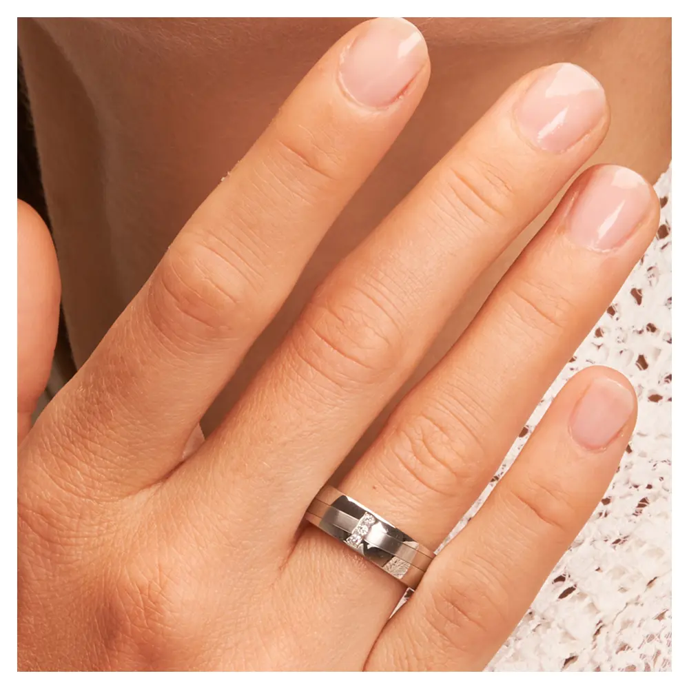 Stahl Eheringe mit 3 Diamanten und schrägem Streifen auf Hand am Gesicht im Zoom