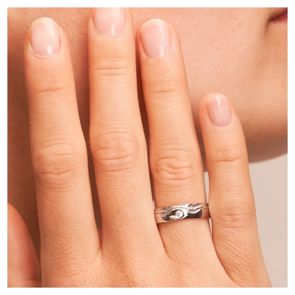 Silber 925 Trauring mit wellig designter Oberfläche und Diamanten auf Hand am Gesicht im Zoom