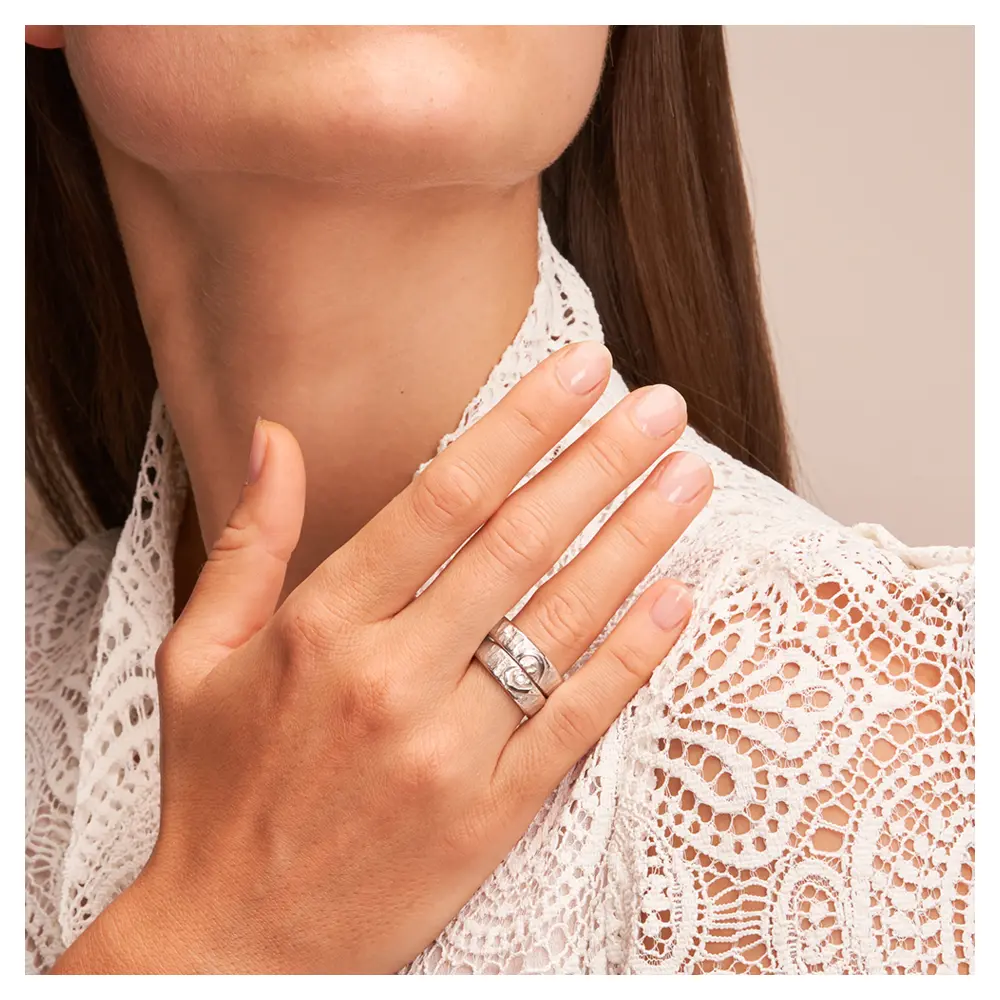 Silber 925 Eheringe mit ringübergreifendem Herz und Diamanten auf Hand am Gesicht