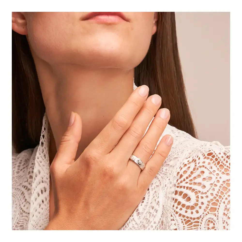 Weißgold Eheringe mit ringübergreifendem Herz und Diamanten auf Hand am Gesicht