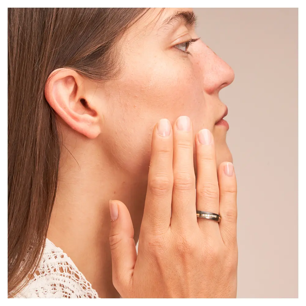 Ehering aus Titan mit Streifen aus Gelbgold und Zirkonium und Diamanten auf Hand am Gesicht 