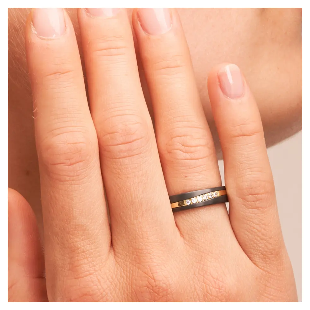 Ehering aus poliertem Gelbgold & dunklem Zirkonium mit 6 Diamanten auf Hand am Gesicht im Zoom