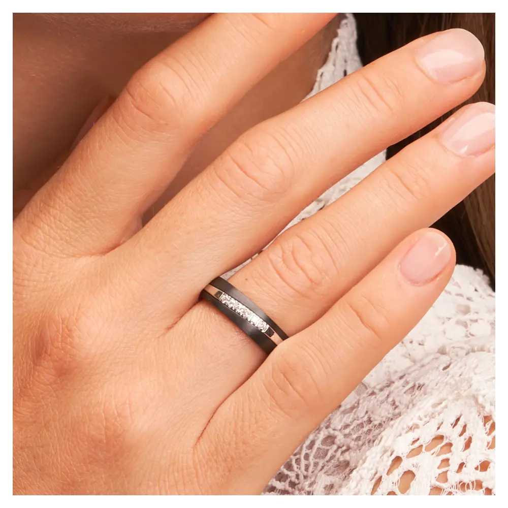 Ehering aus Weißgold & Zirkonium mit 6 Diamanten in bicolorem Design auf Hand am Gesicht im Zoom