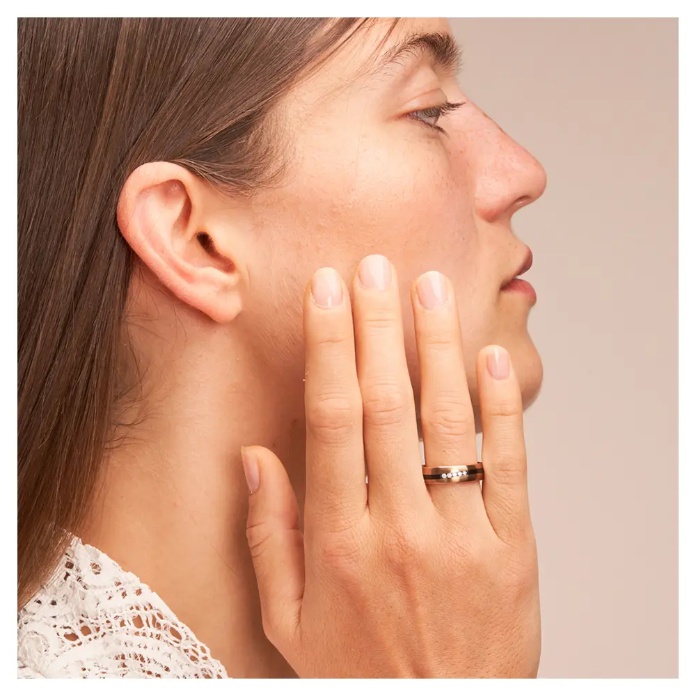Trauring aus Roségold&Zirkonium mit fünf Diamanten und geschwungenem Streifen auf Hand am Gesicht