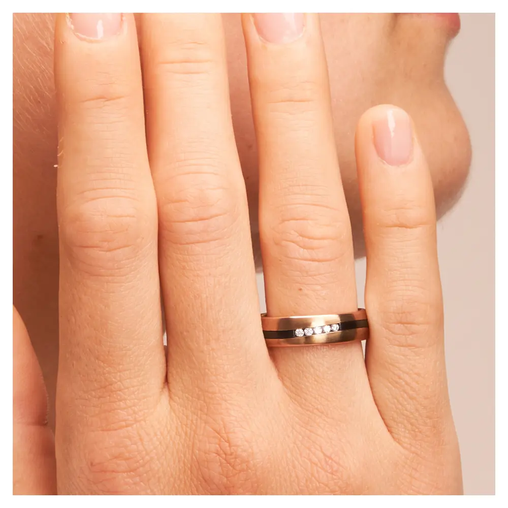 Trauring aus Roségold&Zirkonium mit Diamanten und geschwungenem Streifen auf Hand am Gesicht im Zoom
