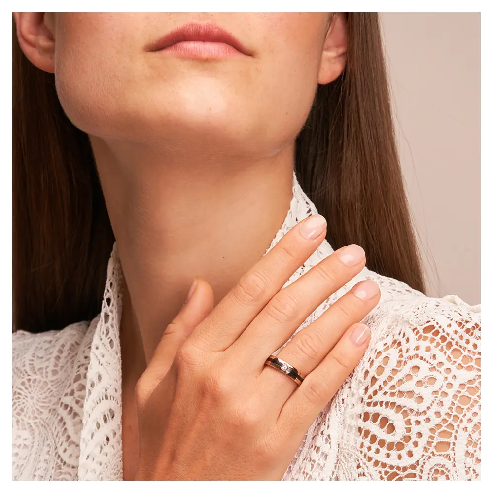 Trauring aus Roségold mit weißem Diamanten und Zirkoniumstreifen auf Hand am Gesicht