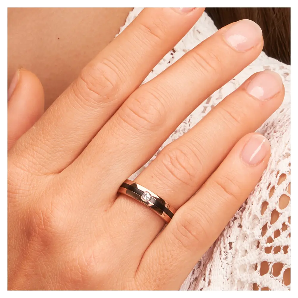 Trauring aus Roségold mit weißem Diamanten und Zirkoniumstreifen auf Hand am Gesicht im Zoom