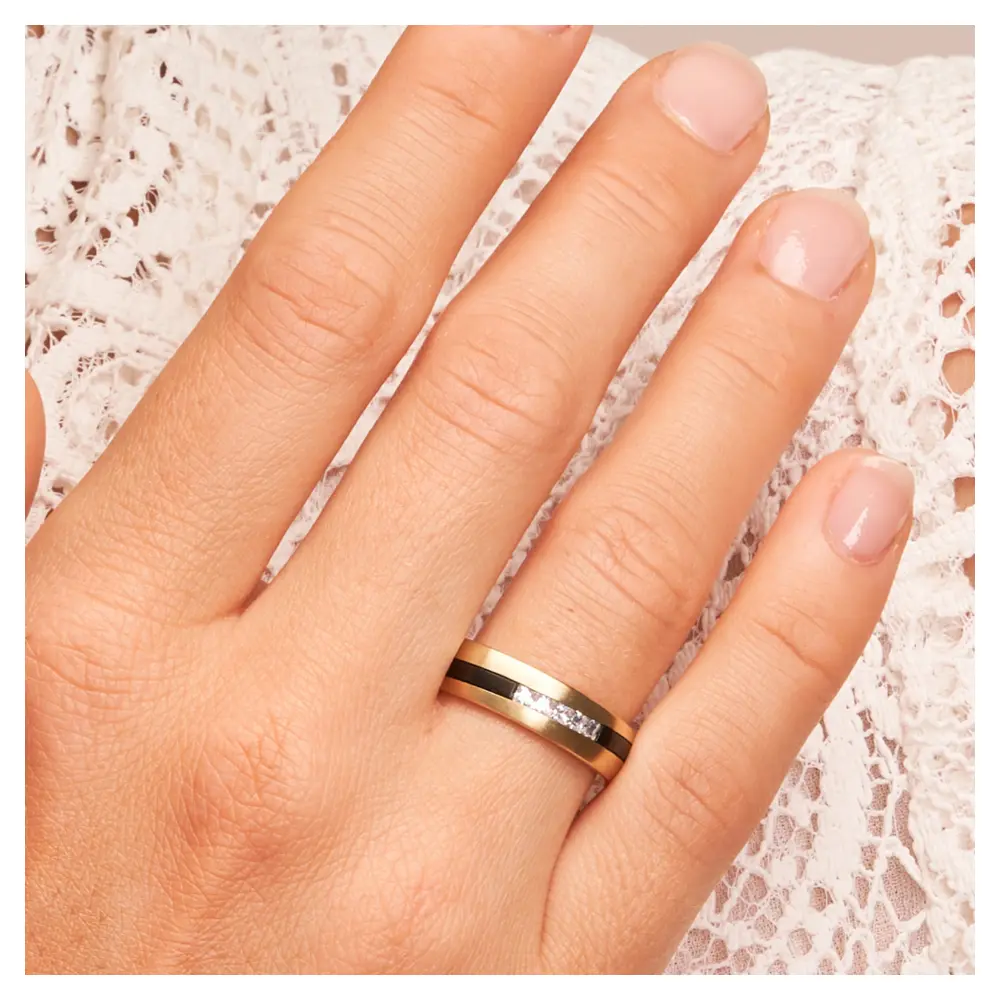 Trauringe aus Gelbgold & Zirkonium bicolor mit fünf Diamanten auf Hand am Gesicht im Zoom