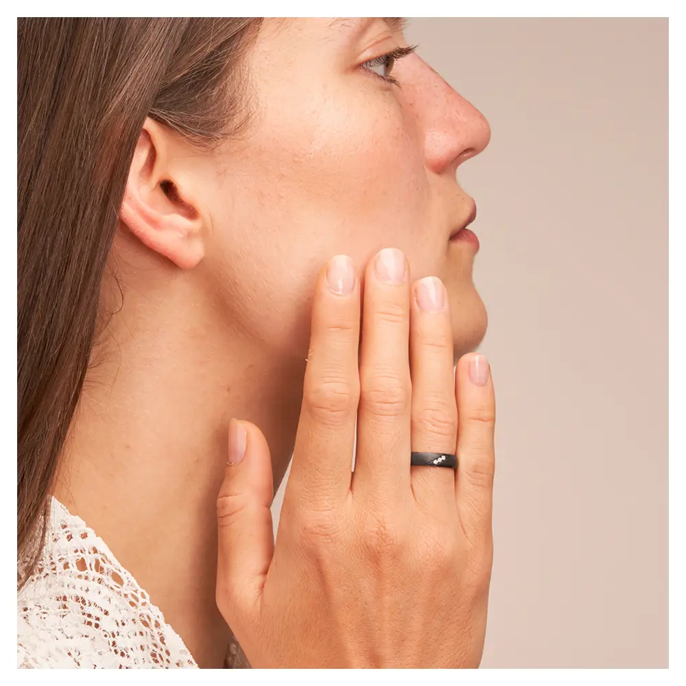 Ehering aus Zirkonium mit 3 Diamanten und besonderer Oberfläche auf Hand am Gesicht