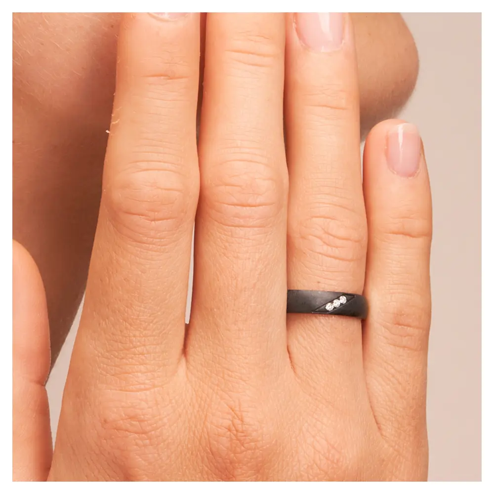 Ehering aus Zirkonium mit 3 Diamanten und besonderer Oberfläche auf Hand am Gesicht im Zoom