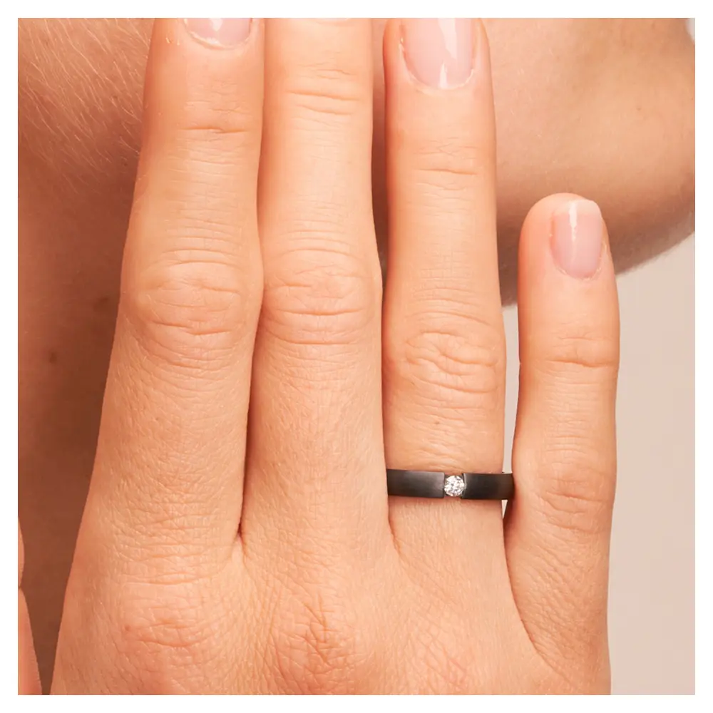 Ehering aus Zirkonium in zwei Breiten mit Diamanten auf Hand am Gesicht im Zoom