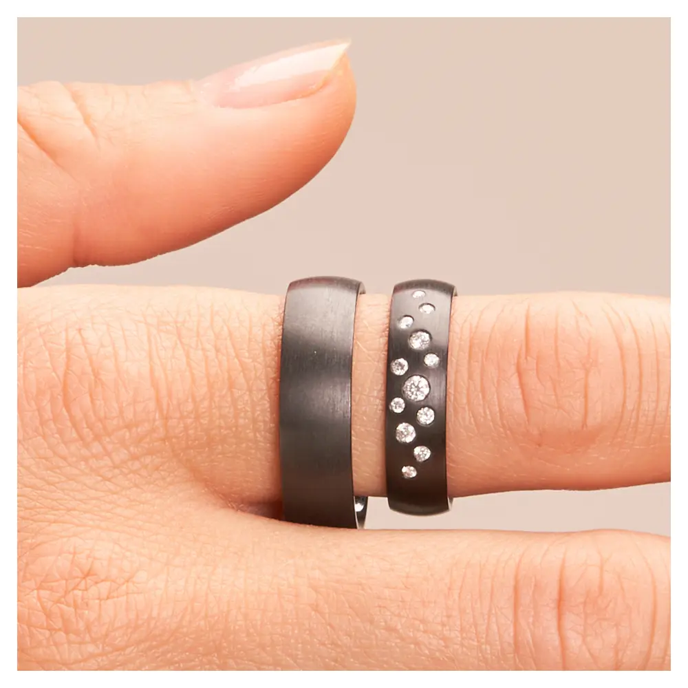 Eheringe aus schwarzem längsmattem Zirkonium mit vielen weißen Diamanten auf Hand im Zoom