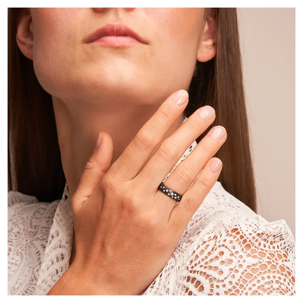 Ehering aus schwarzem längsmattem Zirkonium mit vielen weißen Diamanten auf Hand am Gesicht