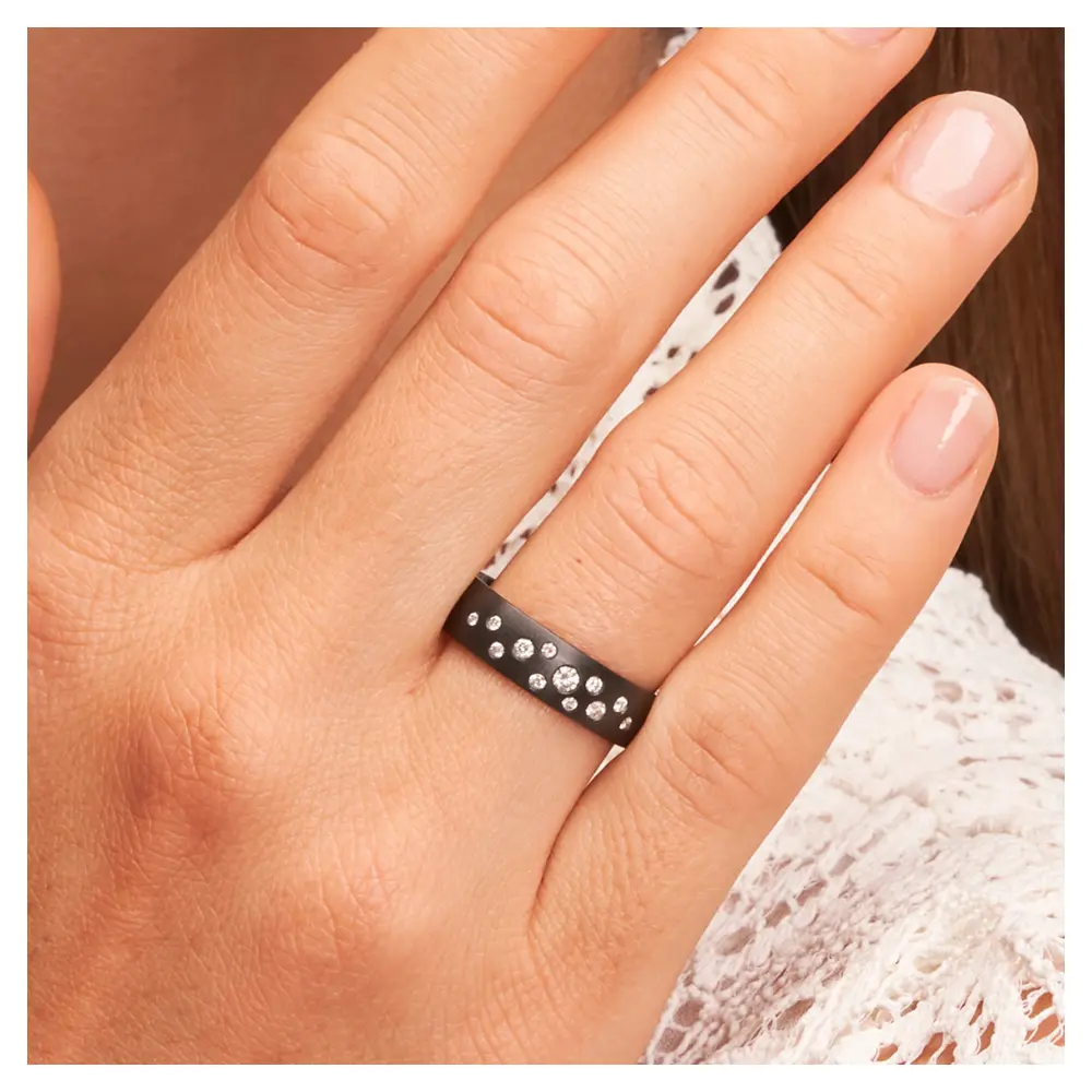 Ehering aus schwarzem längsmattem Zirkonium mit vielen weißen Diamanten auf Hand am Gesicht im Zoom