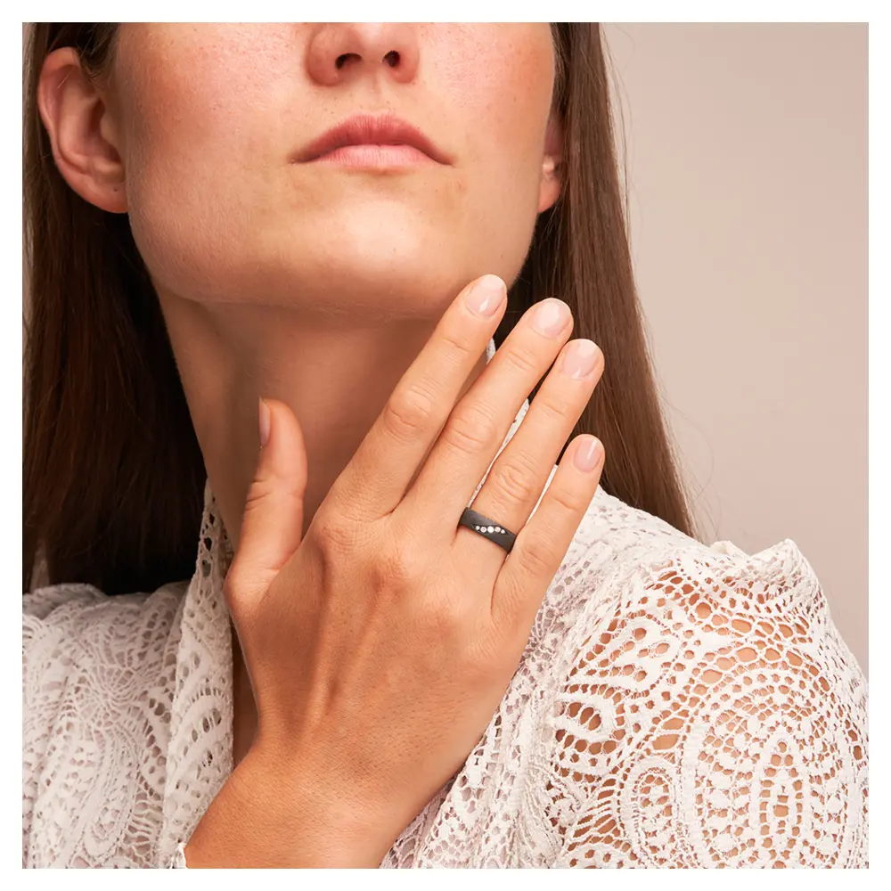Schimmernder schwarzer Ehering aus Zirkonium mit fünf Diamanten auf Hand am Gesicht