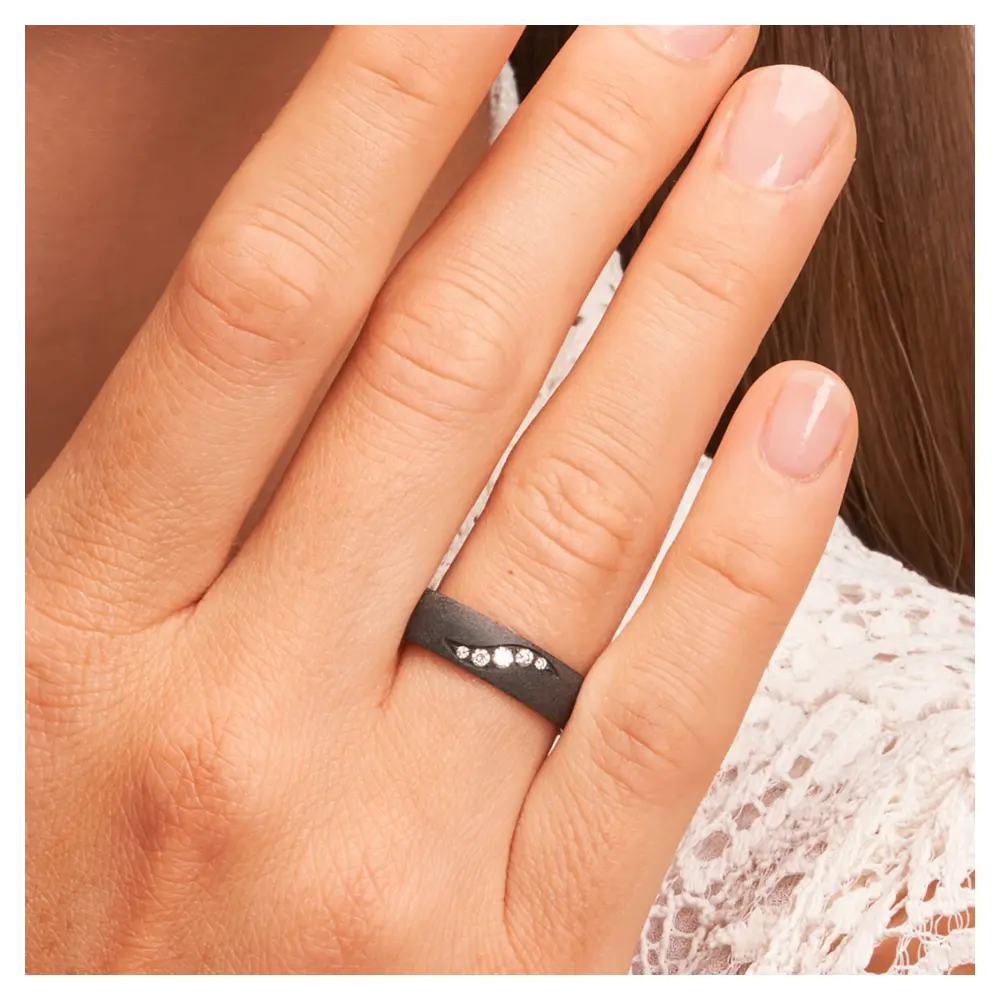 Schimmernder schwarzer Ehering aus Zirkonium mit fünf Diamanten auf Hand am Gesicht im Zoom