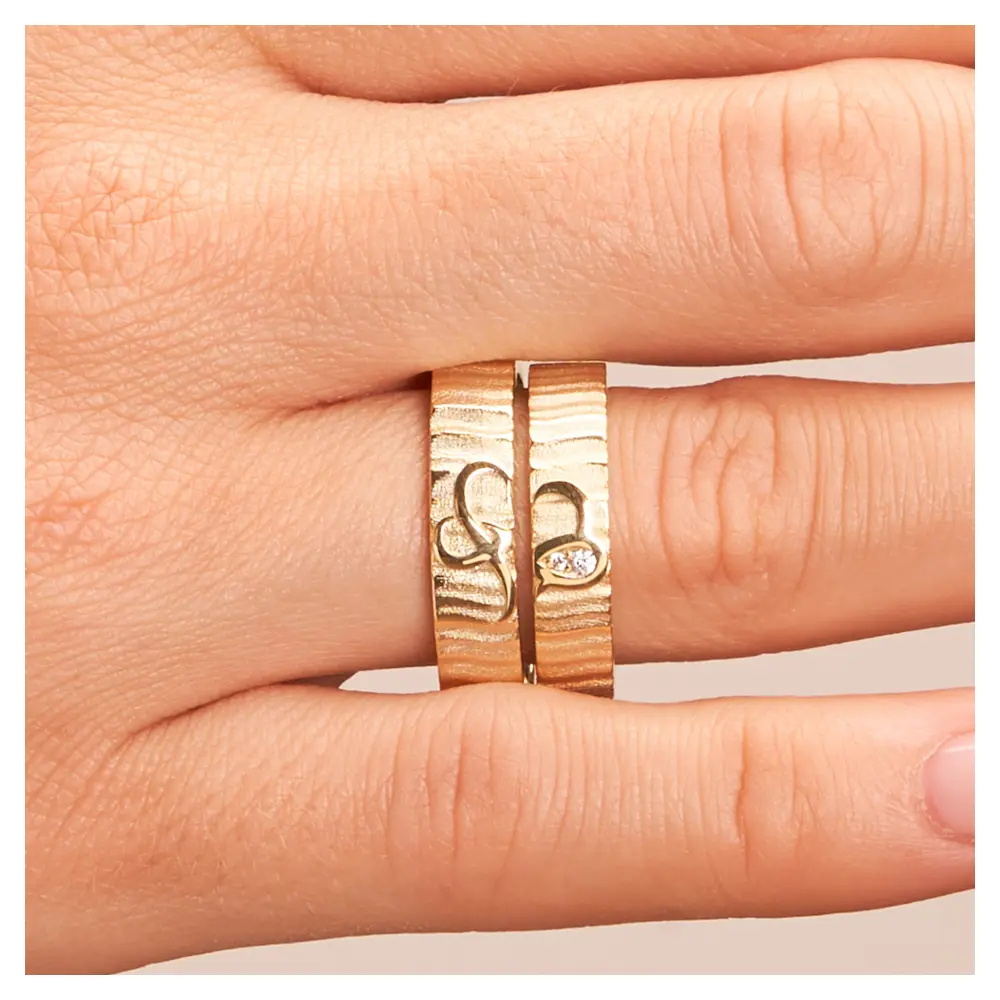 Eheringe aus Gelbgold mit geriffelter Oberfläche und zwei Diamanten auf Hand im Zoom