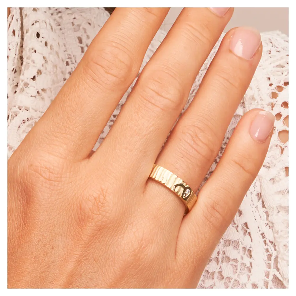Ehering aus Gelbgold mit geriffelter Oberfläche und zwei Diamanten auf Hand am Gesicht im Zoom