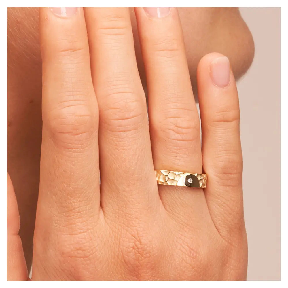 Ehering aus Gelbgold in Hammerschlag-Optik und Yin & Yang-Symbol auf Hand am Gesicht im Zoom