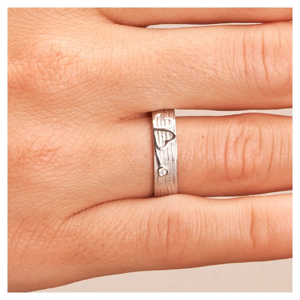 Ehering aus Weißgold mit einem Kleeblatt als Symbol und Diamant auf Hand im Zoom