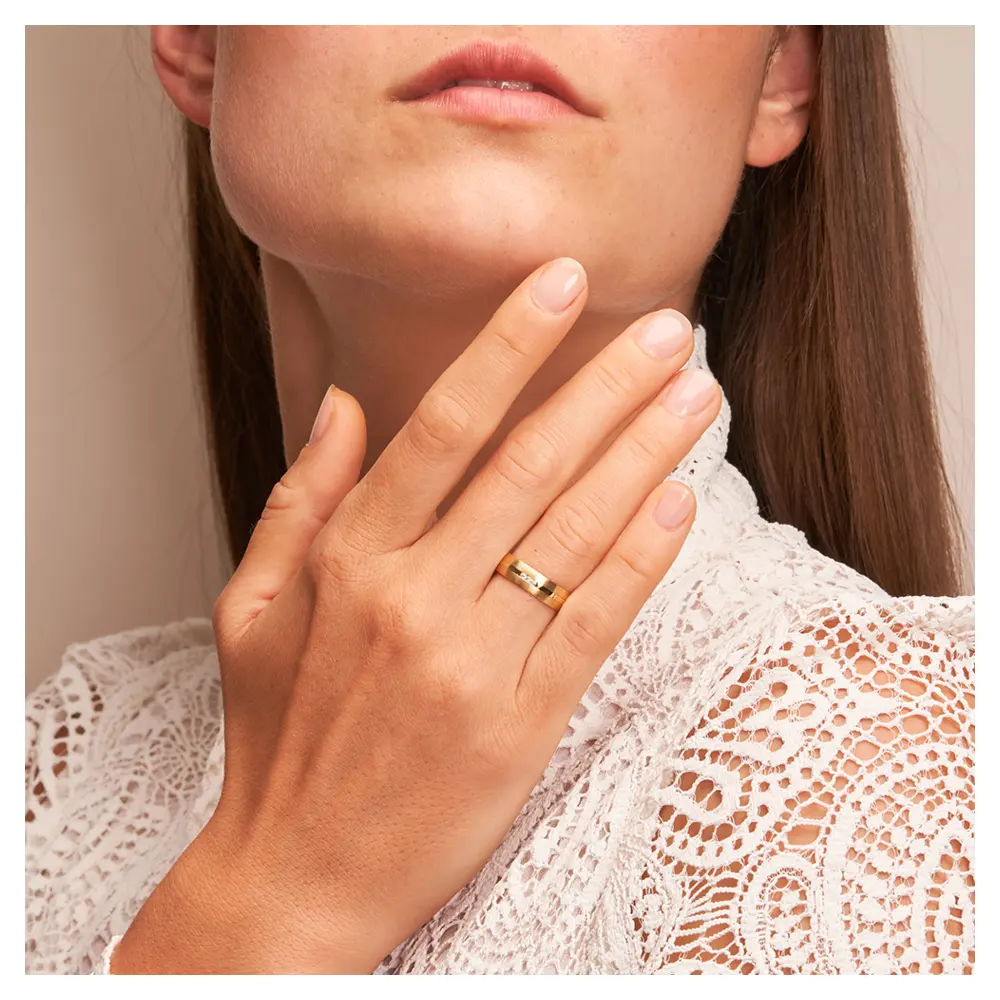 Eheringe aus Gelbgold mit Diamanten und matter Oberfläche auf Hand am Gesicht