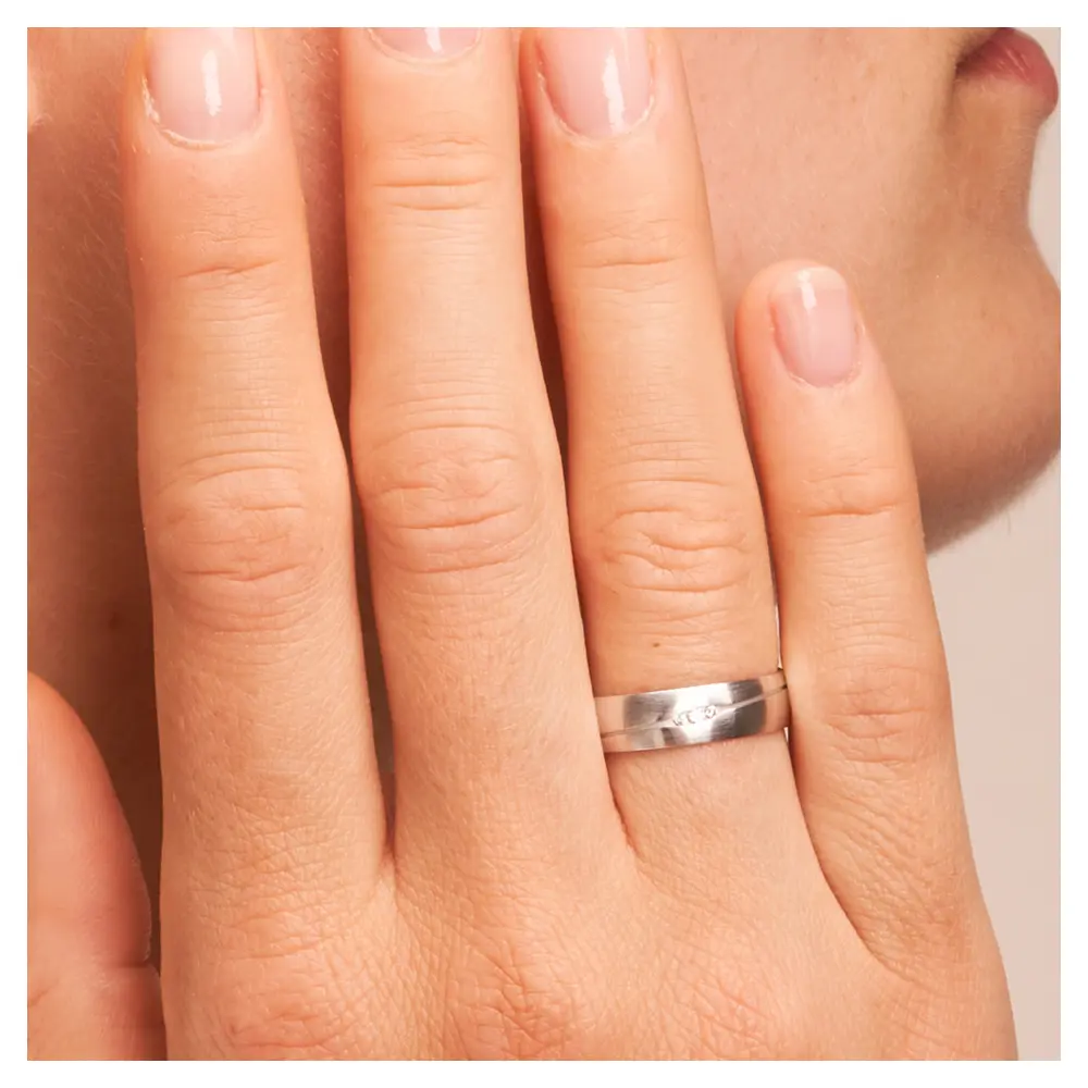 Längsmattierte Eheringe aus Weissgold mit ovaler Rille und Diamanten auf Hand am Gesicht im Zoom