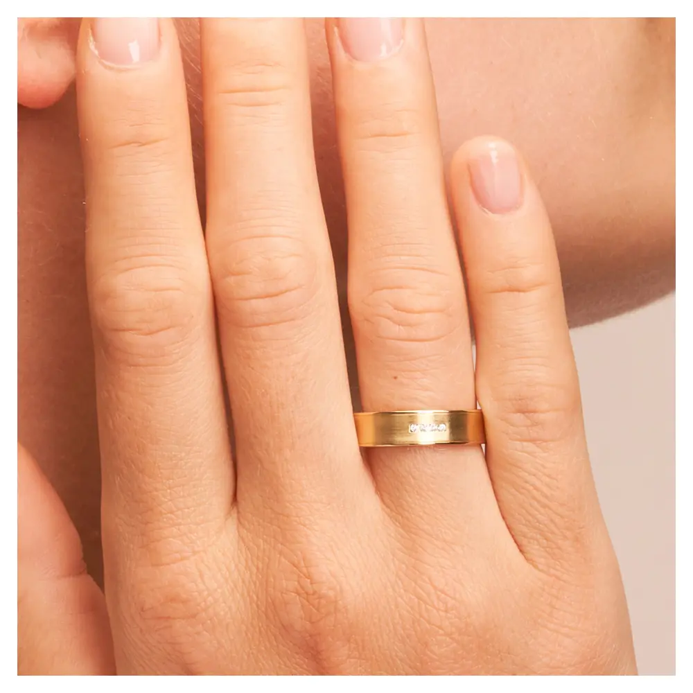 Konkave Eheringe aus Gelbgold mit Diamanten und polierten Rändern auf Hand am Gesicht im Zoom