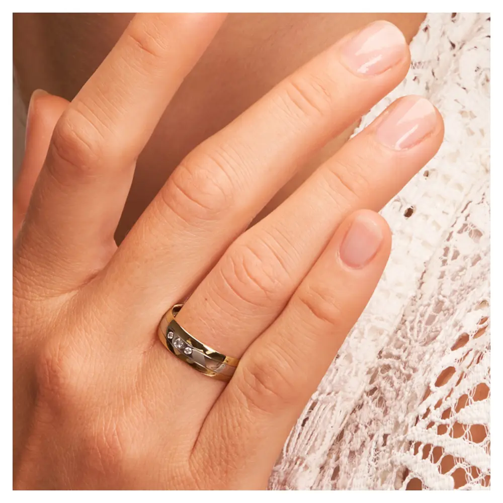 Trauring aus Palladium 500 & Gelbgold mit drei runden Diamanten auf Hand am Gesicht im Zoom