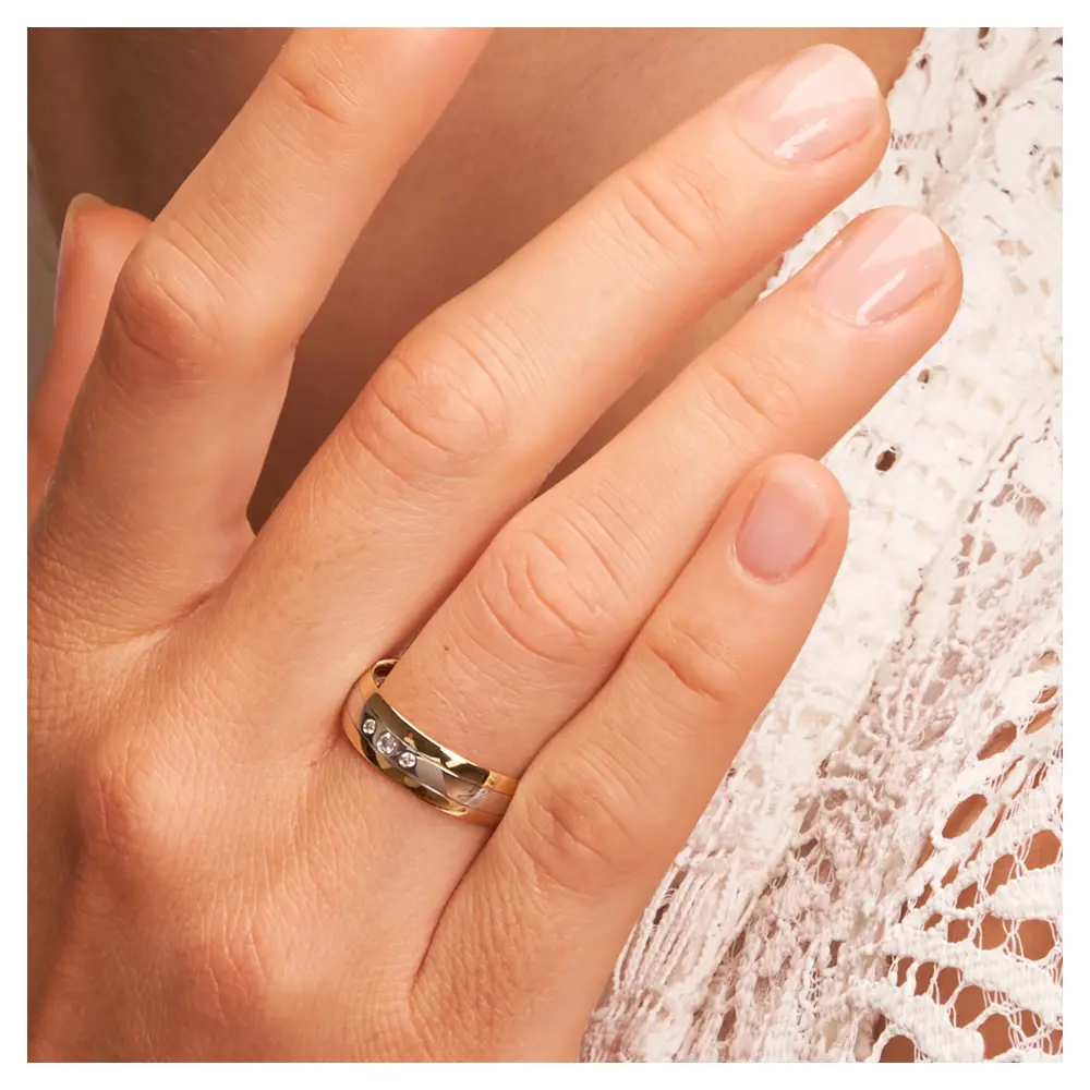 Trauring aus Weißgold und Gelbgold mit glänzenden Diamanten auf Hand am Gesicht im Zoom