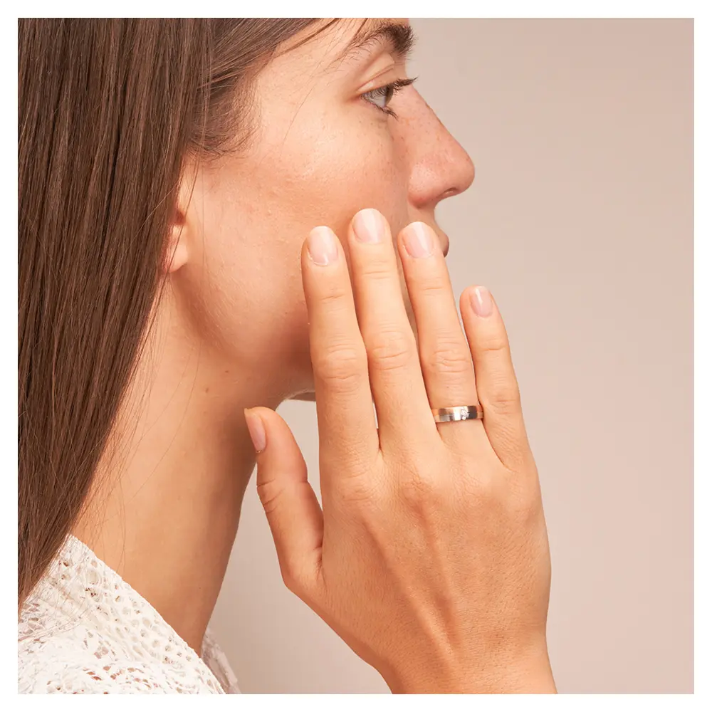 Trauring in Rotgold/Weißgold längsmattitert mit Diamanten auf Hand am Gesicht