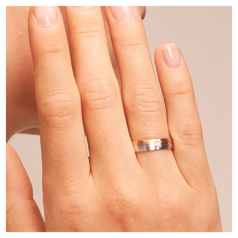 Trauring in Rotgold/Weißgold längsmattitert mit Diamanten auf Hand am Gesicht im Zoom