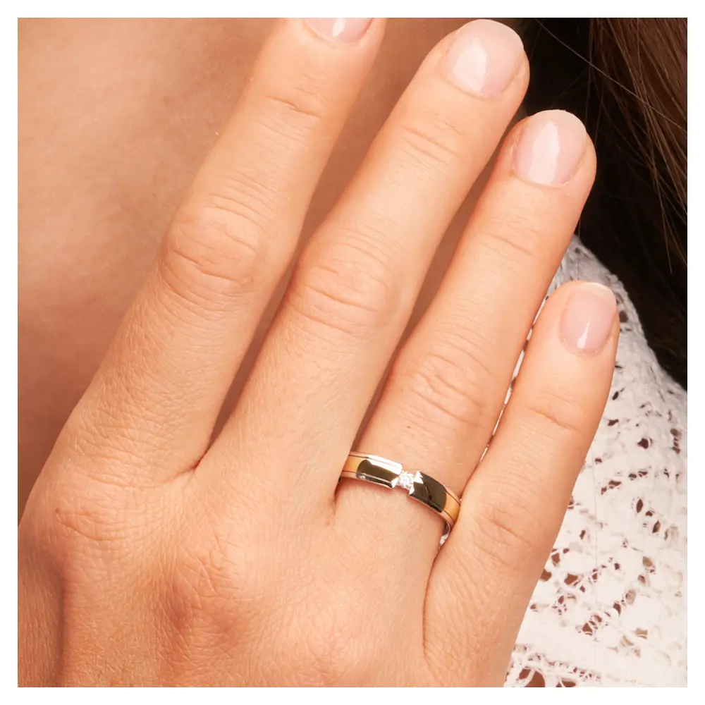 Ehering aus Weißgold und Gelbgold mit rundem Diamanten auf Hand am Gesicht im Zoom