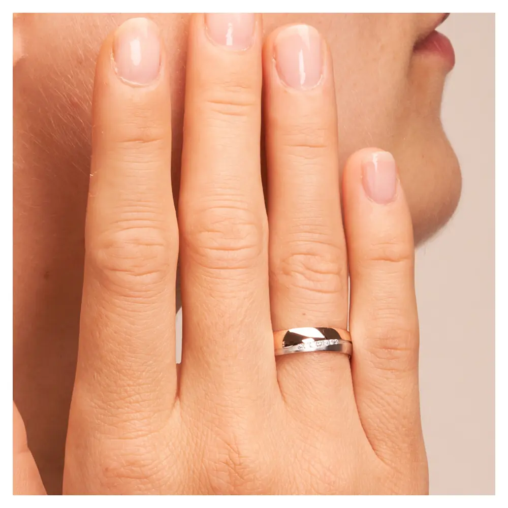 Ehering in poliertem Rotgold und mattem Weißgold mit 7 Diamanten auf Hand am Gesicht im Zoom