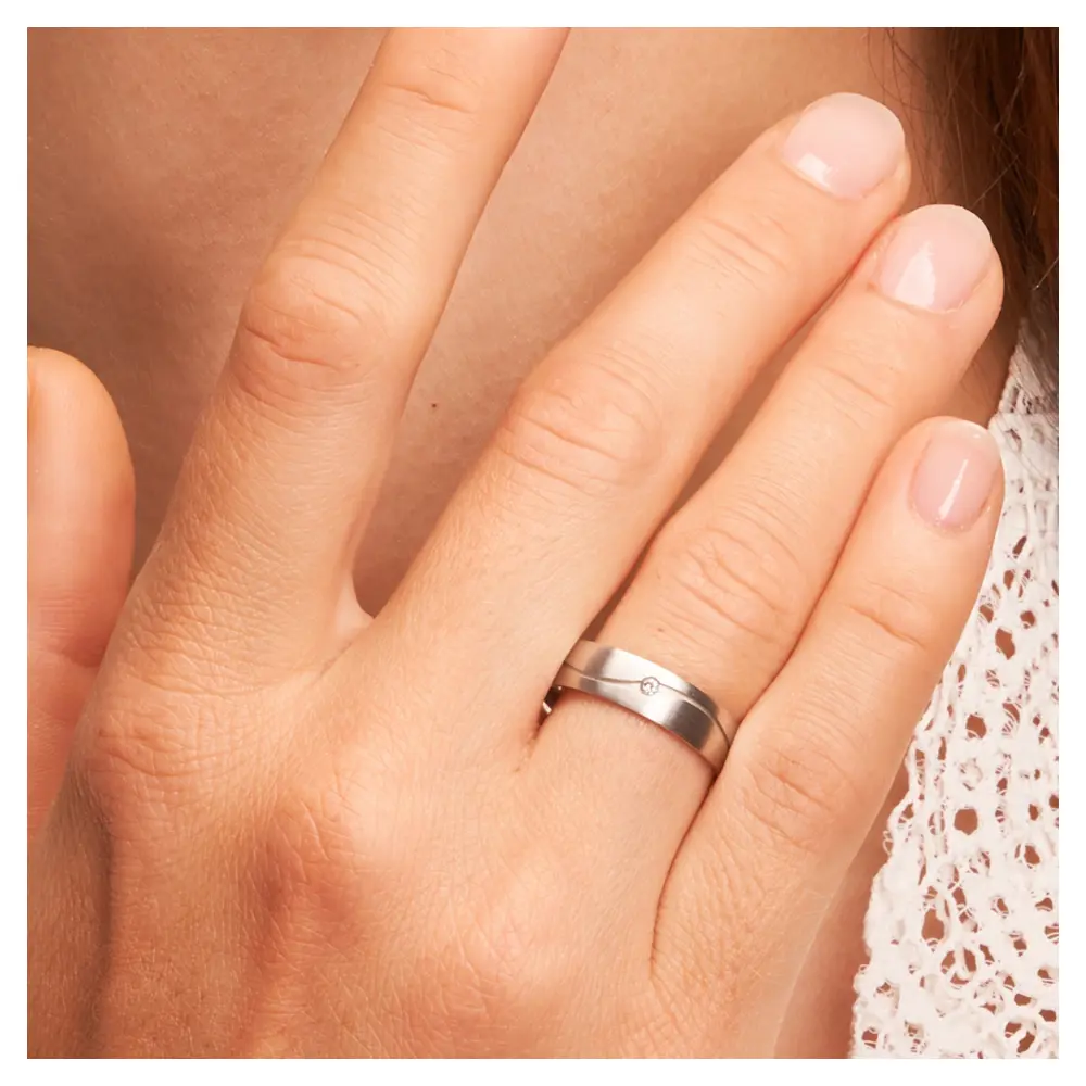 Längsmatte Eheringe aus Weißgold mit Rille und Diamanten auf Hand am Gesicht im Zoom