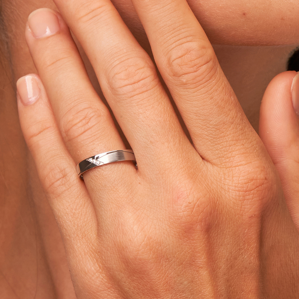 Eheringe aus Platin mit geschwungener Rille und 3 Diamanten auf Hand am Gesicht in Nahaufnahme