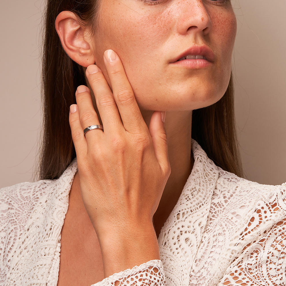 Eheringe aus Platin mit geschwungener Rille und 3 Diamanten auf Hand am Gesicht